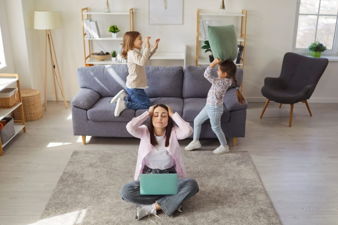 Gestresste Mutter mit Laptop, im Hintergrund zwei streitende Kinder