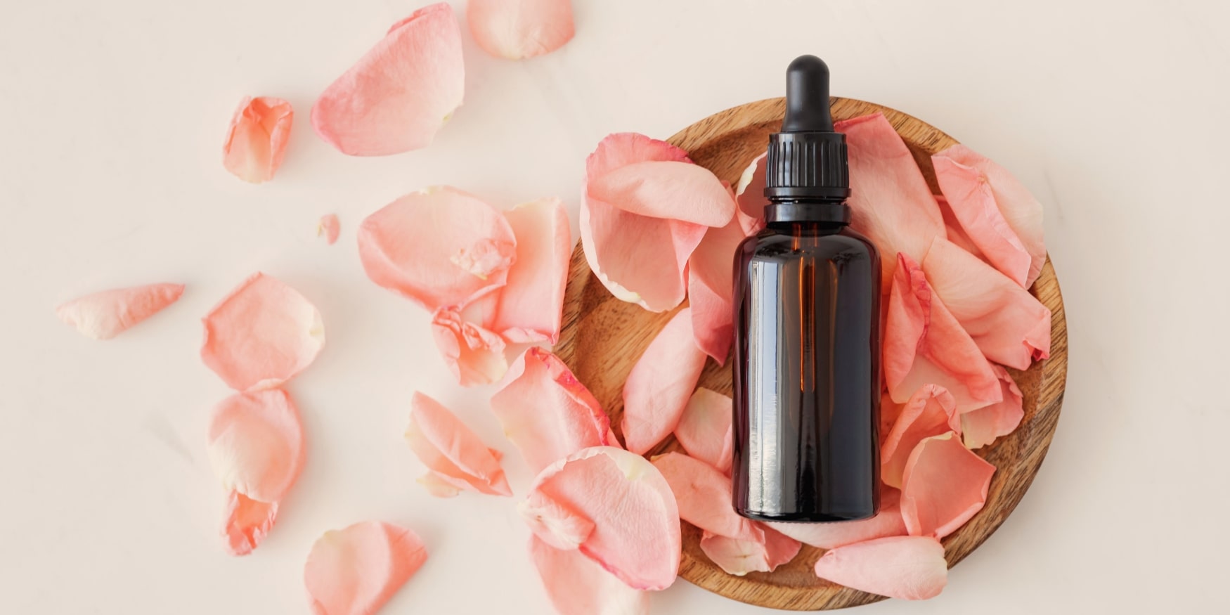 Flasche aus Braunglas mit ätherischem Öl auf einem Tisch voller Rosenblätter