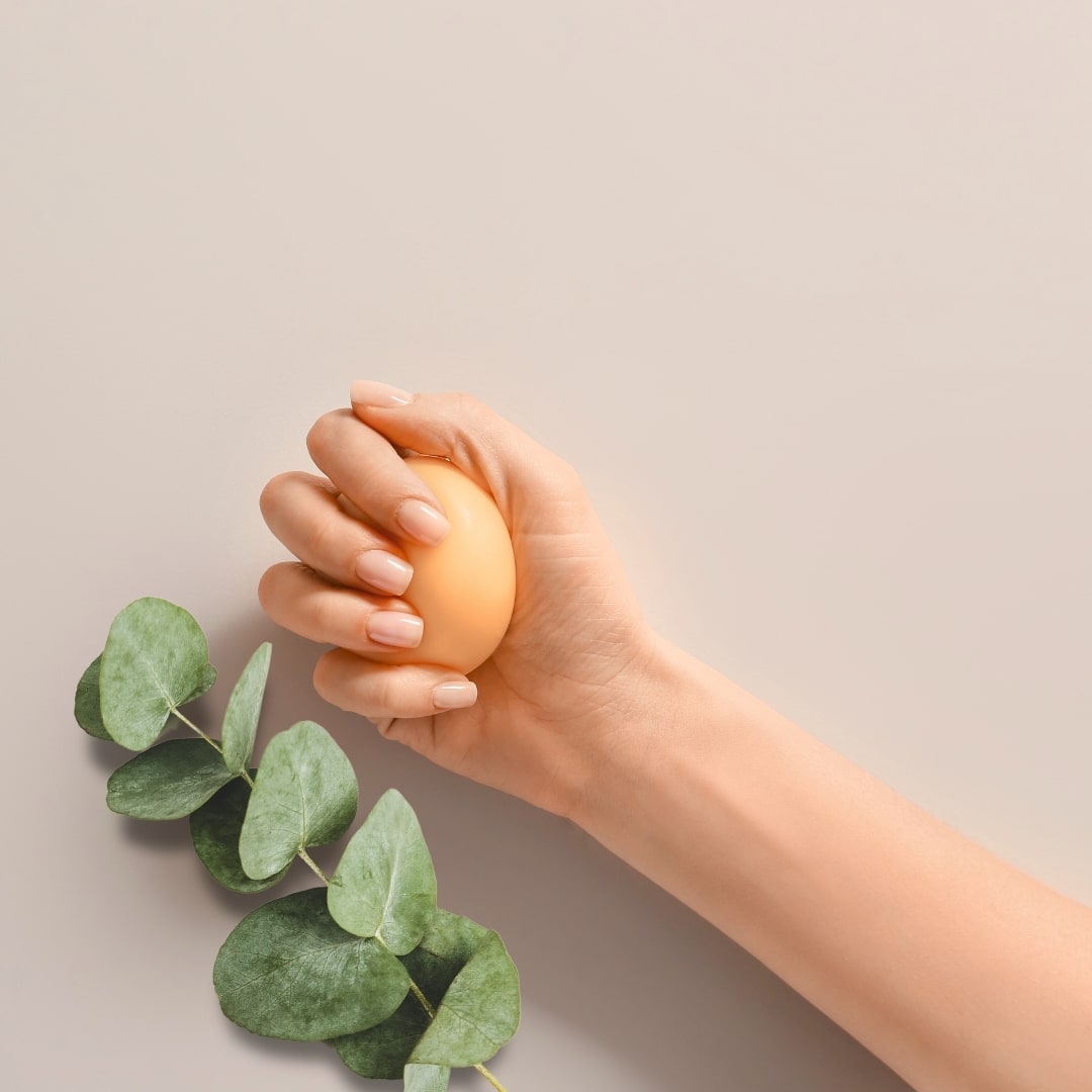 Hand knetet die orangefarbene Zendou Duftknete "Energy", daneben ein grüner Zweig